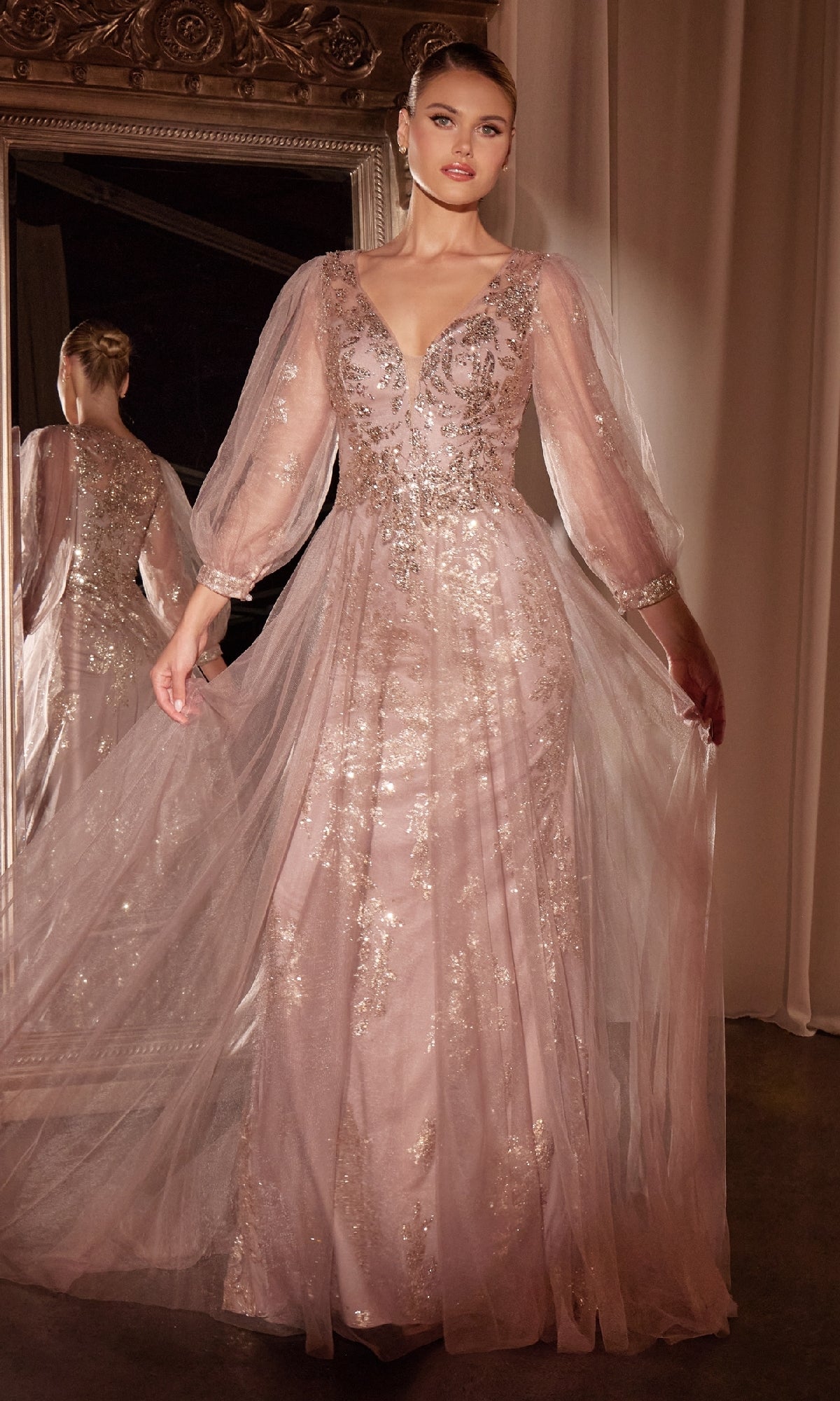 A person stands in front of a mirror wearing the Ladivine CD0102 Sheer-Sleeve Long Prom Dress—a light pink, sparkling A-line gown with sheer sleeves and embellished details.